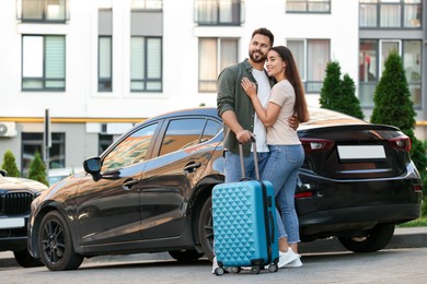 Photo of Long-distance relationship. Beautiful young couple with suitcase hugging near car outdoors