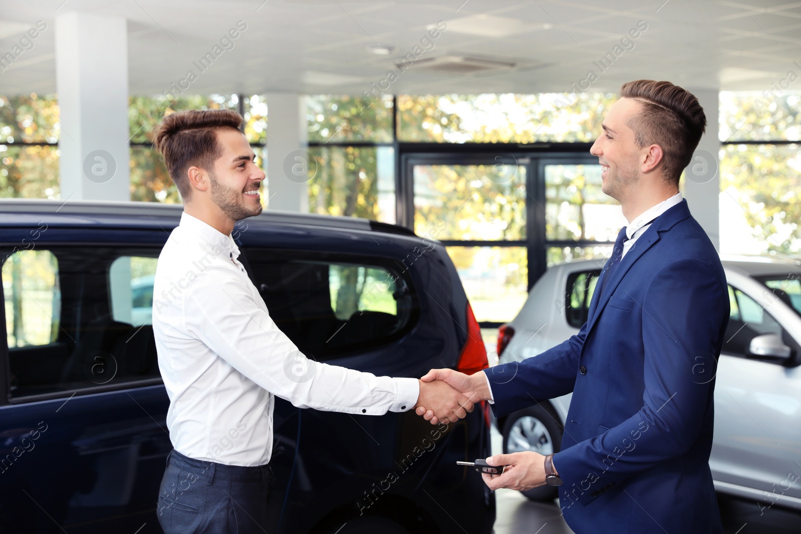 Photo of Young car salesman shaking hands with client in dealership