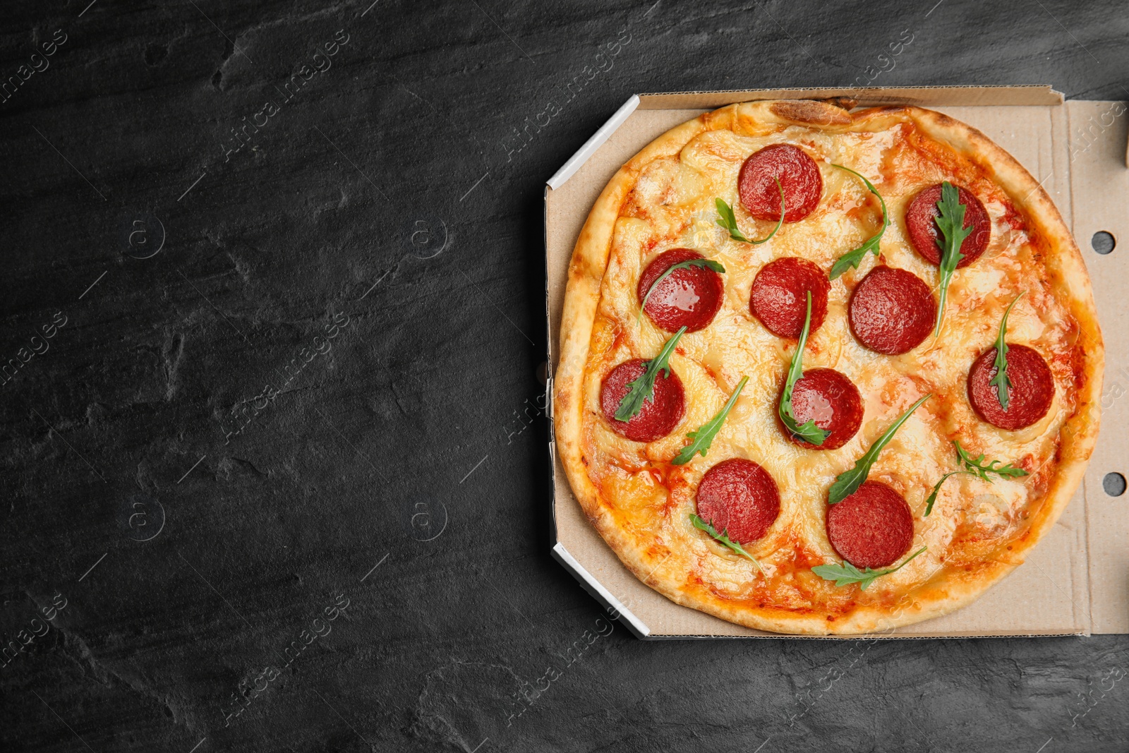 Photo of Tasty pepperoni pizza in cardboard box on black table, top view. Space for text