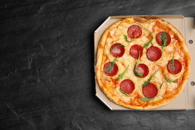 Photo of Tasty pepperoni pizza in cardboard box on black table, top view. Space for text