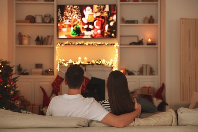 Photo of Couple watching Christmas movie via TV in cosy room, back view. Winter holidays atmosphere