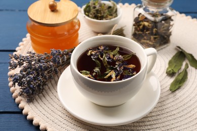 Aromatic tea with different dry herbs and honey on blue wooden table, closeup