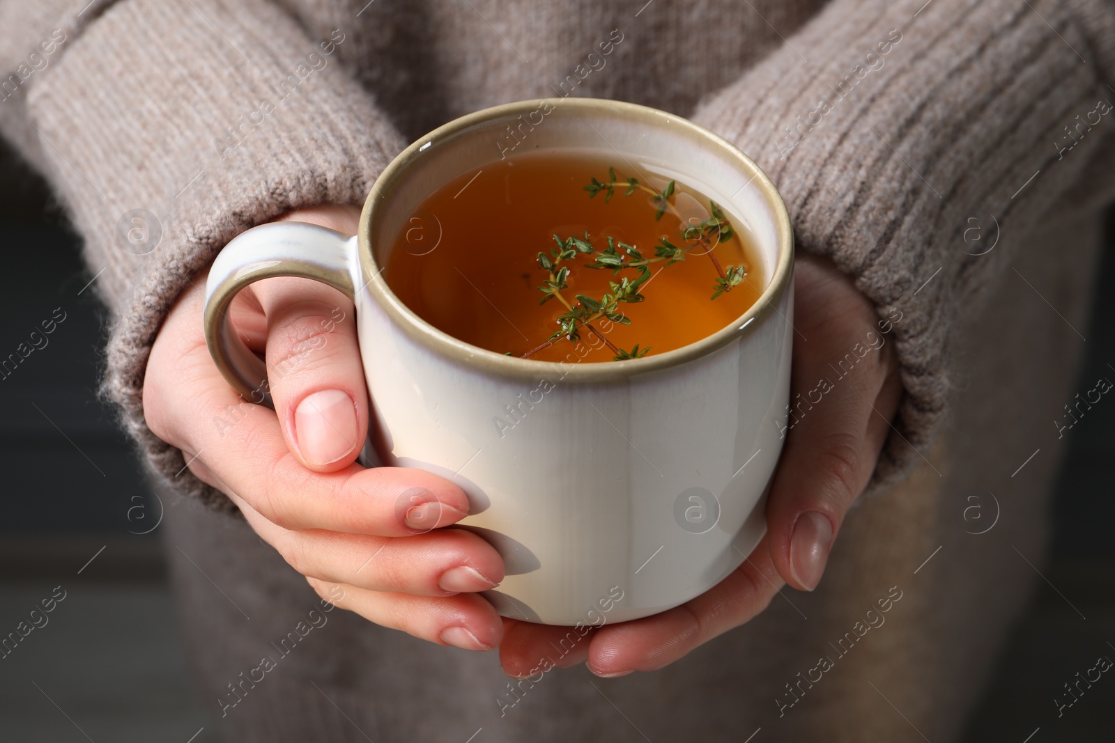 Photo of Woman holding cup of tasty herbal tea with thyme, closeup