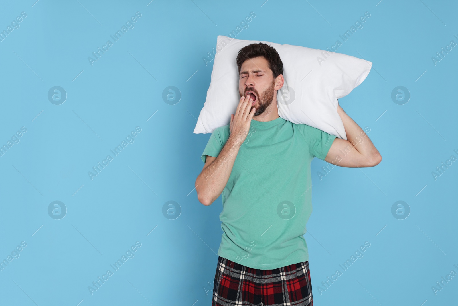 Photo of Tired man with pillow yawns on light blue background, space for text
