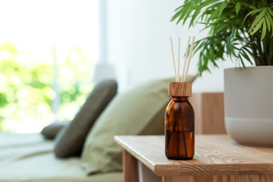 Aromatic reed air freshener near houseplant on wooden table indoors. Space for text