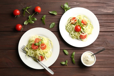 Photo of Tasty zucchini pasta with tomatoes and basil served on wooden table, flat lay