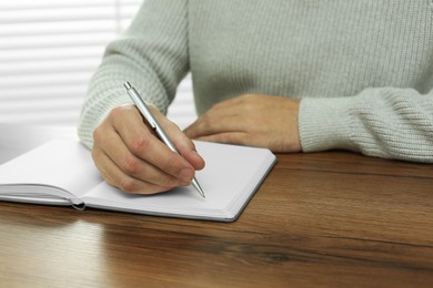 Photo of Man writing in notebook at wooden table indoors, closeup