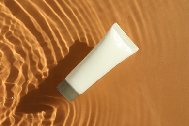 Photo of Tube with moisturizing cream in water on orange background, top view