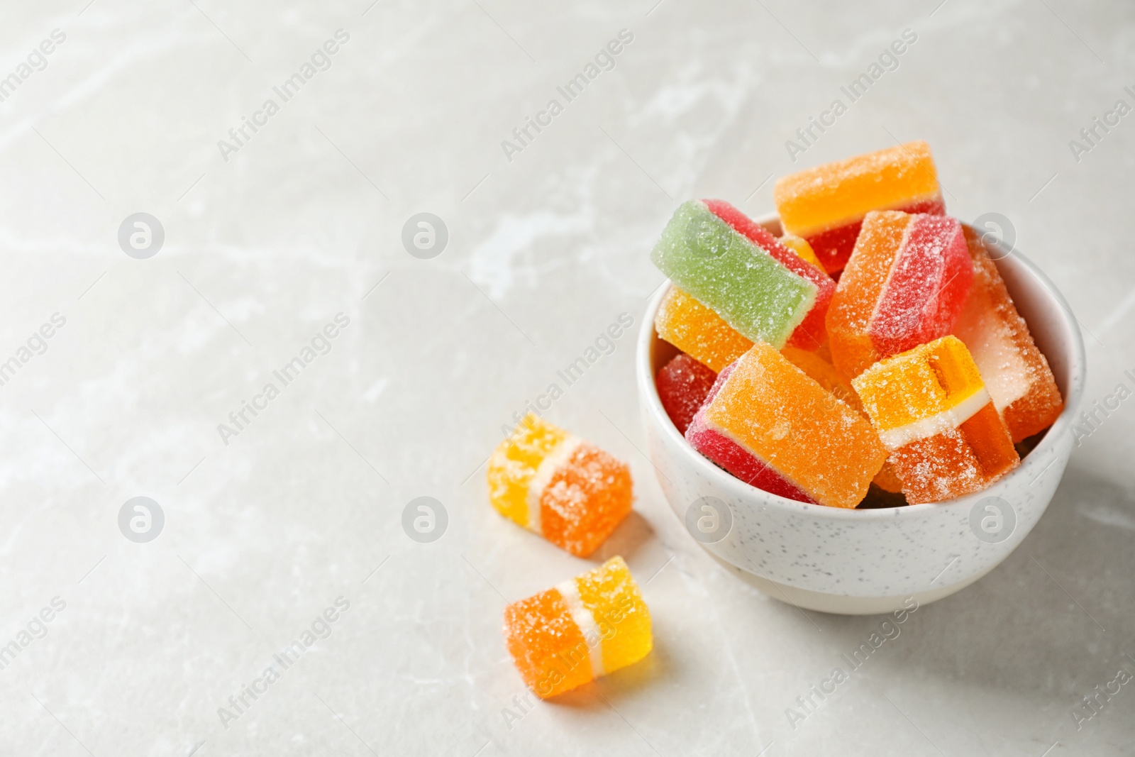 Photo of Bowl of delicious colorful candies on gray table with space for text