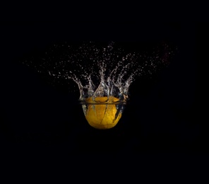 Ripe lemon falling down into clear water with splashes against black background