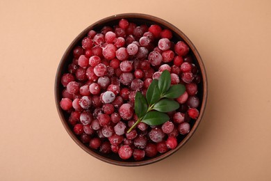 Frozen red cranberries and green leaves on beige background, top view