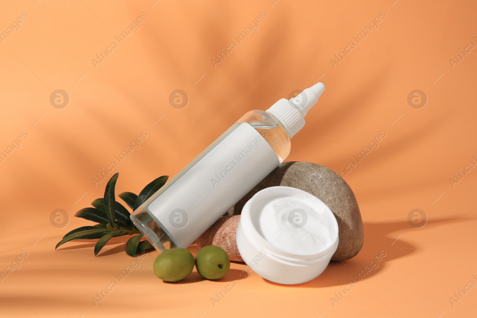 Photo of Cosmetic products and olives on orange background