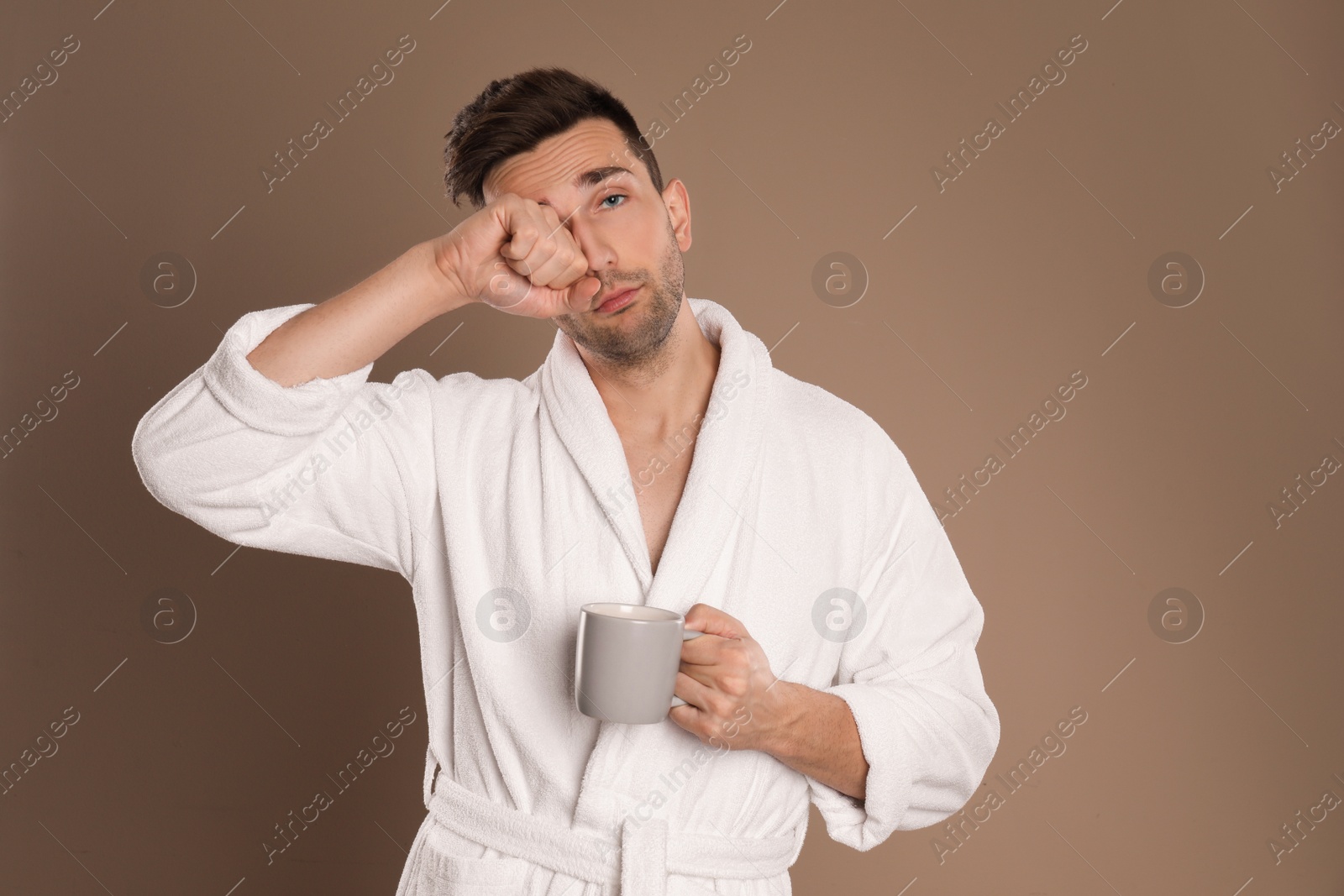 Photo of Young man in bathrobe with cup of coffee on brown background