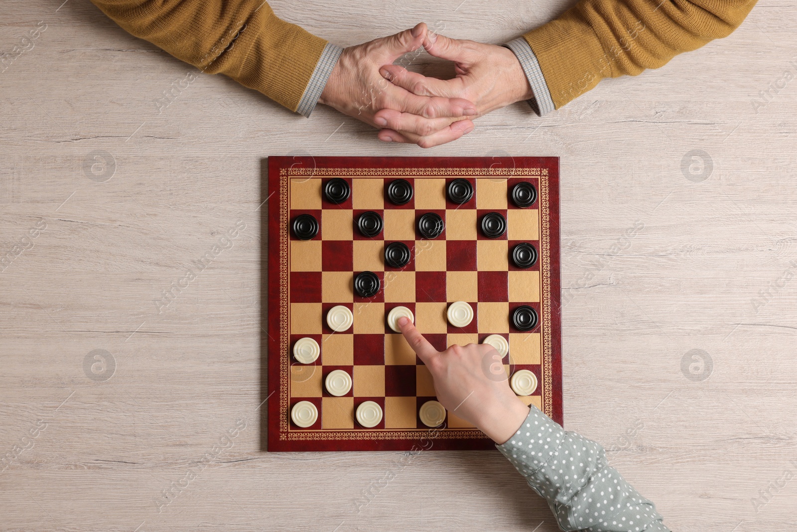 Photo of Senior man playing checkers with woman at white wooden table, top view