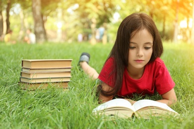 Photo of Cute little girl reading book on green grass in park