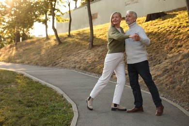 Affectionate senior couple dancing together outdoors, space for text