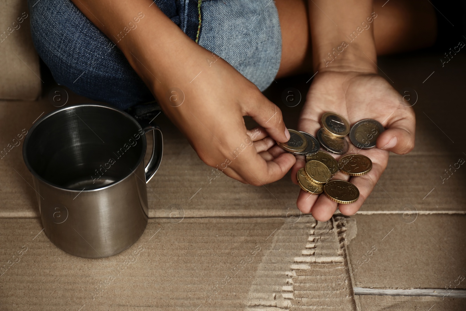 Photo of Poor boy counting coins over cardboard on floor, closeup