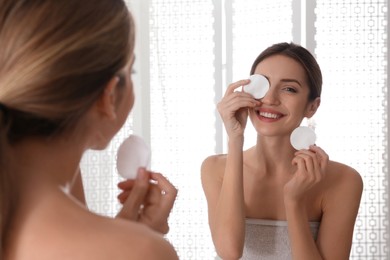 Young woman with cotton pads cleaning her face near mirror in bathroom