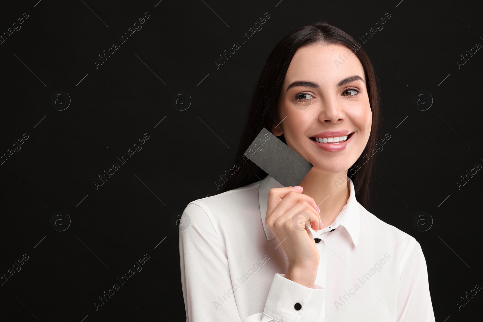 Photo of Happy woman holding blank business card on black background. Space for text