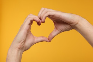 Photo of Man showing heart gesture with hands on golden background, closeup