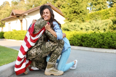 Man in military uniform with American flag hugging his wife outdoors