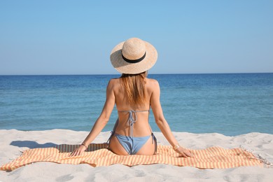 Photo of Woman sitting on beach towel near sea, back view