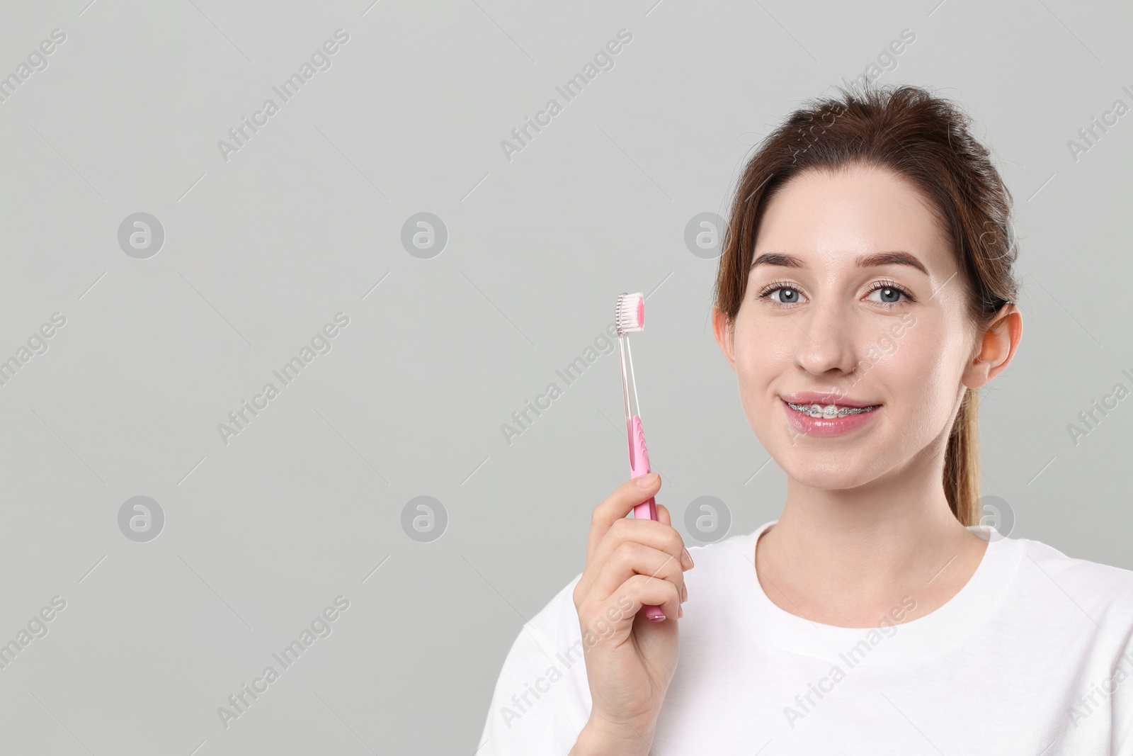 Photo of Portrait of smiling woman with dental braces and toothbrush on grey background. Space for text