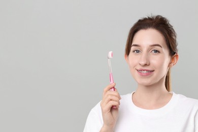 Portrait of smiling woman with dental braces and toothbrush on grey background. Space for text