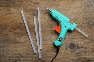 Turquoise glue gun and sticks on wooden table, flat lay