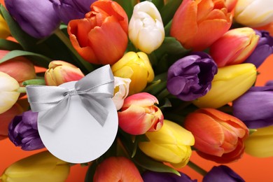 Photo of Bouquet of beautiful colorful tulips with blank card on orange background, closeup. Birthday celebration