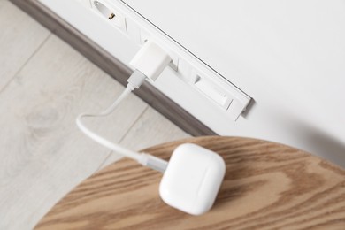 Photo of Modern wireless earphones charging from electric socket indoors, above view