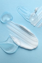 Samples of cosmetic gel and cream on light blue background, top view