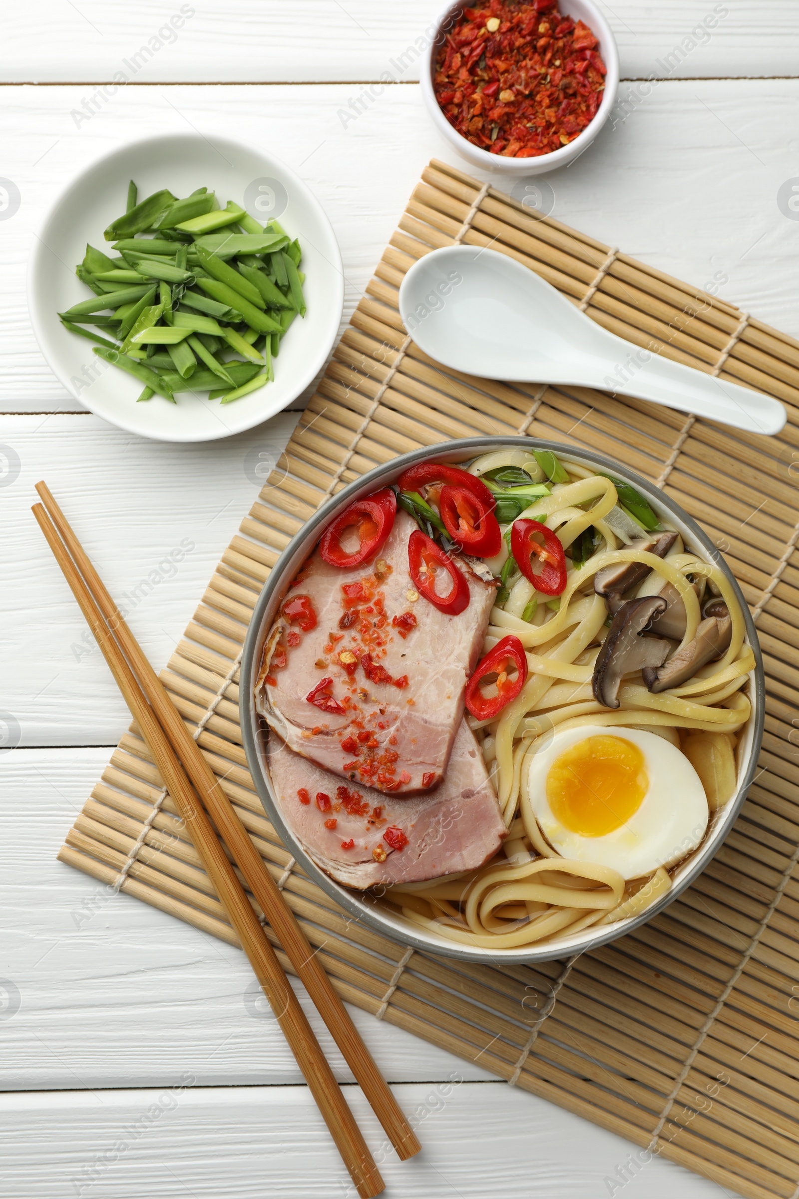 Photo of Delicious ramen in bowl served on white wooden table, flat lay. Noodle soup