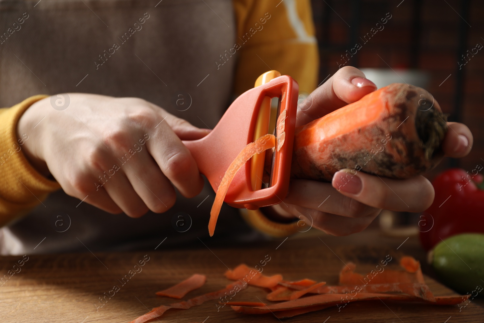 Photo of Woman peeling fresh carrot at wooden table indoors, closeup