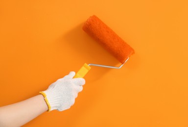 Designer painting orange wall with roller, closeup