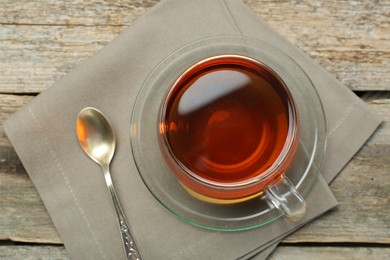 Photo of Aromatic tea in glass cup, spoon and napkin on wooden table, top view