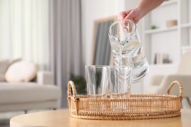 Woman pouring fresh water from jug into glass at wooden table indoors, closeup. Space for text