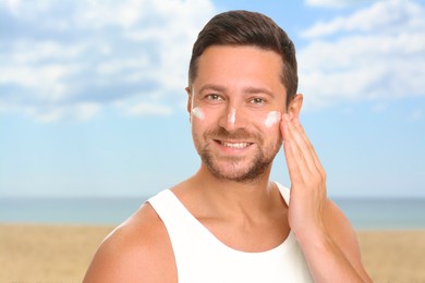 Image of Sun protection. Man applying sunblock onto face on beach