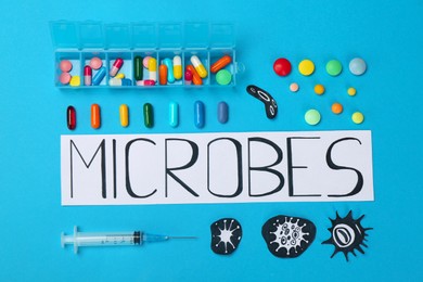 Photo of Card with word Microbes, colorful pills, pictures and syringe on light blue background, flat lay