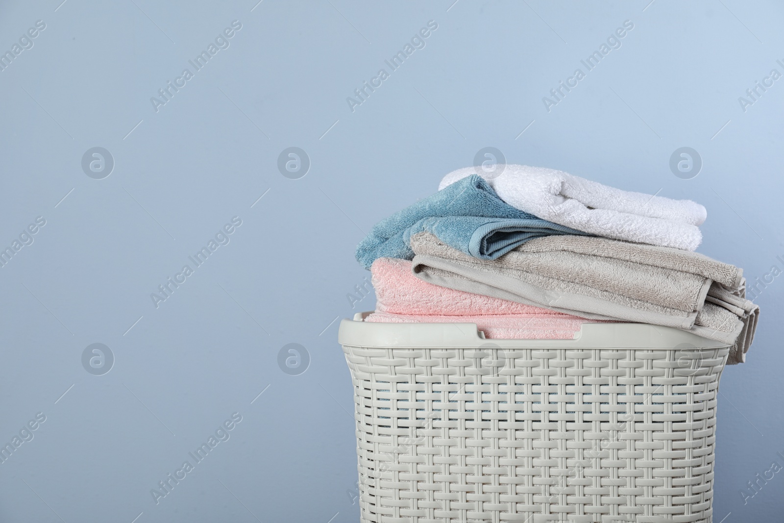 Photo of Laundry basket with clean towels on color background. Space for text