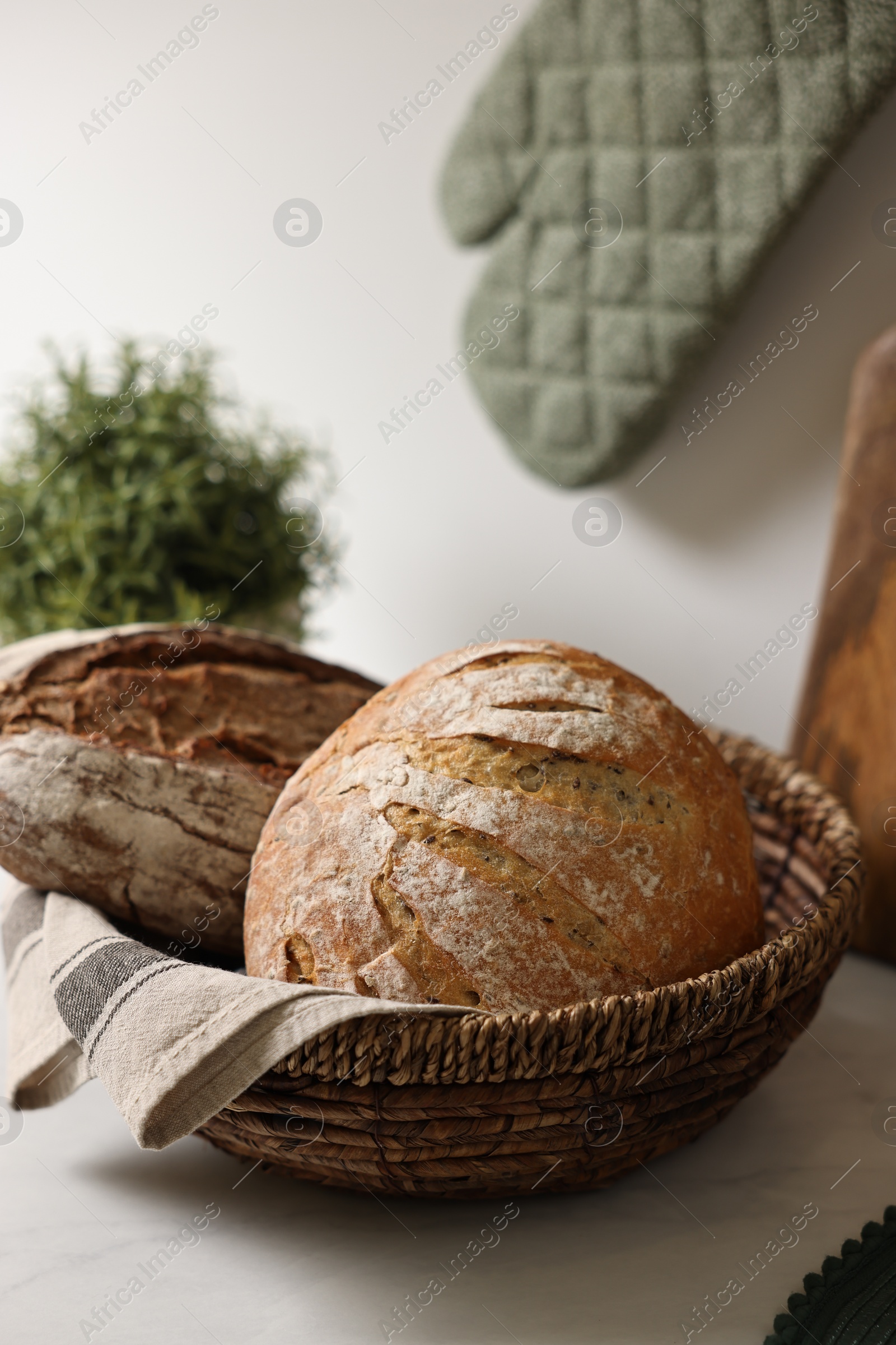 Photo of Wicker bread basket with freshly baked loaves on white marble table in kitchen