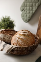 Wicker bread basket with freshly baked loaves on white marble table in kitchen