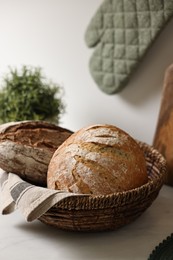 Photo of Wicker bread basket with freshly baked loaves on white marble table in kitchen