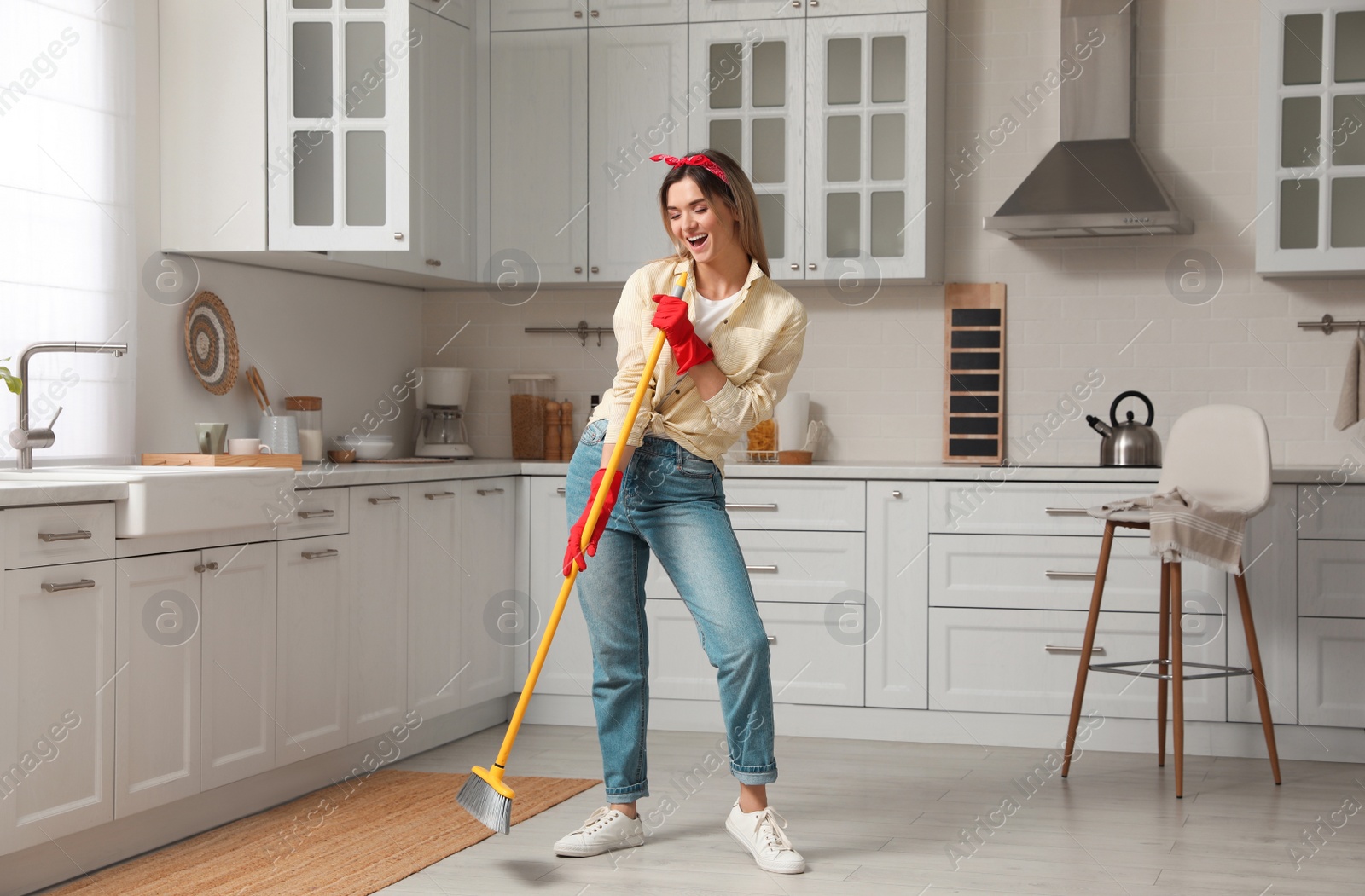 Photo of Woman with broom singing while cleaning in kitchen