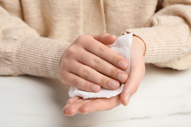 Woman wiping hands with paper towel at white marble table, closeup