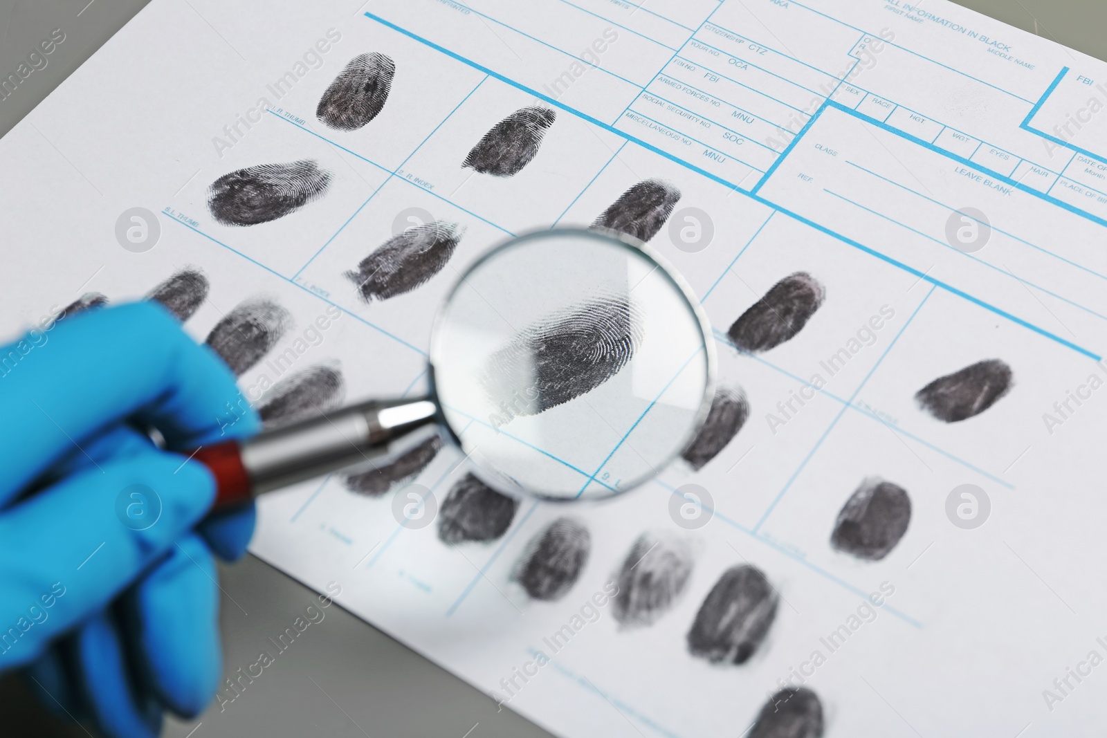 Photo of Criminalist exploring fingerprints with magnifying glass, closeup