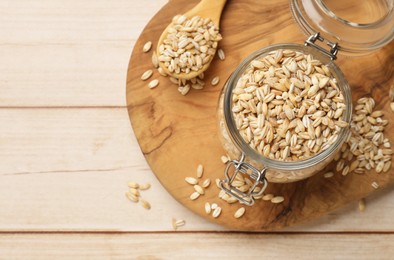 Photo of Dry pearl barley in glass jar and spoon on light wooden table, top view. Space for text