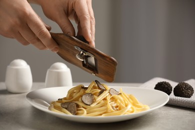 Photo of Woman slicing truffle onto fettuccine at grey table, closeup