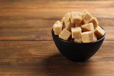 Photo of Brown sugar cubes on wooden table, space for text