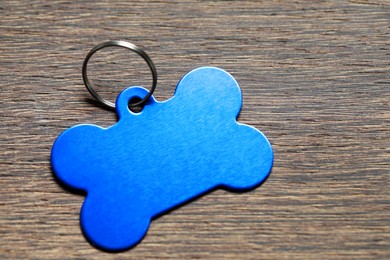 Photo of Light blue metal pet tag in shape of bone with ring on wooden table, closeup. Space for text